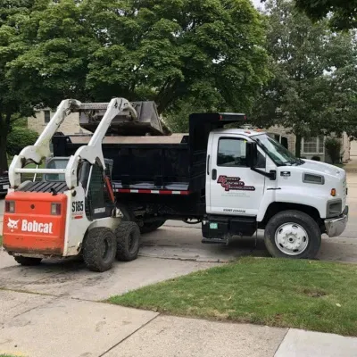Waukesha concrete removal service using a Bobcat loader and dump truck for efficient debris transport
